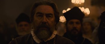 Movie still from “The Last Duel” (2021), directed by Ridley Scott – An old man with a beard and a necklace is looking at the camera; Close Up shot, Over the shoulder angle