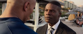 Movie still from “Baywatch” (2017), directed by Seth Gordon – A man wearing a suit and tie talking to another man; Close Up shot, Over the shoulder angle
