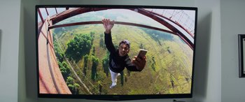 Movie still from “Baywatch” (2017), directed by Seth Gordon – A man hanging from the side of a bridge holding a cell phone up in the air; Wide shot, Overhead angle