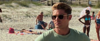 Movie still from “Baywatch” (2017), directed by Seth Gordon – A man with sunglasses on a beach with other people; Close Up shot, Over the shoulder angle