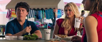Movie still from “Baywatch” (2017), directed by Seth Gordon – A woman sitting at a table with a sandwich and a drink; Medium shot, Over the shoulder angle