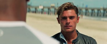 Movie still from “Baywatch” (2017), directed by Seth Gordon – A person with a surfboard on the beach; Close Up shot, Over the shoulder angle