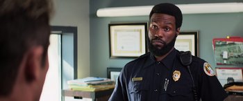 Movie still from “Baywatch” (2017), directed by Seth Gordon – A man in a police uniform standing next to a desk; Close Up shot, Over the shoulder angle
