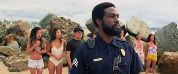 Movie still from “Baywatch” (2017), directed by Seth Gordon – A man that is standing in front of a group of people; Medium shot, Over the shoulder angle