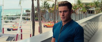 Movie still from “Baywatch” (2017), directed by Seth Gordon – A man in a blue shirt standing in front of palm trees; Close Up shot, Over the shoulder angle
