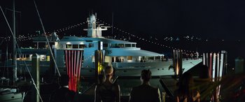 Movie still from “Baywatch” (2017), directed by Seth Gordon – Two people sitting on a dock looking at a large boat; Extreme Wide shot, High angle