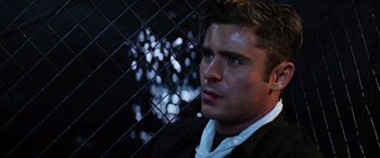 Movie still from “Baywatch” (2017), directed by Seth Gordon – A person wearing a suit near a chain link fence; Close Up shot, High angle