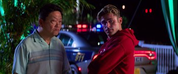 Movie still from “Baywatch” (2017), directed by Seth Gordon – Two men standing next to each other in front of a police car at night; Medium shot, Over the shoulder angle