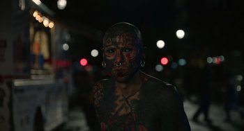 Movie still from “Beau Is Afraid” (2023), directed by Ari Aster – A person with tattoos and piercings on their face and neck; Close Up shot, High angle