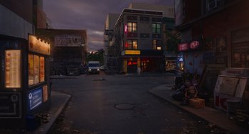 Movie still from “Beau Is Afraid” (2023), directed by Ari Aster – A city street at night with people sitting on the side of the road; Extreme Wide shot, High angle
