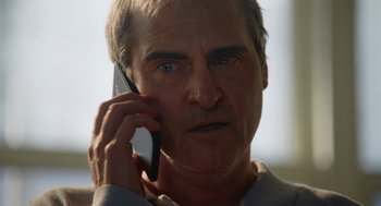 Movie still from “Beau Is Afraid” (2023), directed by Ari Aster – An older man talking on a cell phone; Close Up shot, Low angle