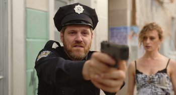 Movie still from “Beau Is Afraid” (2023), directed by Ari Aster – A man in a police uniform is holding a gun; Close Up shot, Low angle