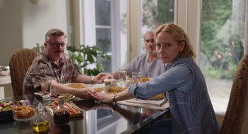Movie still from “Beau Is Afraid” (2023), directed by Ari Aster – A group of people sitting at a table with plates of food on it; Medium shot, Over the shoulder angle