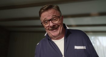 Movie still from “Beau Is Afraid” (2023), directed by Ari Aster – An older man with a mustache wearing glasses and a blue jacket; Close Up shot, Low angle