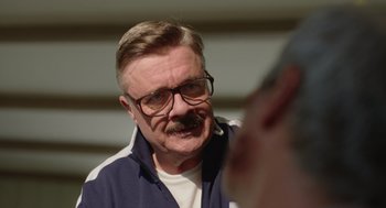 Movie still from “Beau Is Afraid” (2023), directed by Ari Aster – An older man wearing glasses and a mustache; Close Up shot, Over the shoulder angle