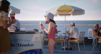 Movie still from “Beau Is Afraid” (2023), directed by Ari Aster – A woman in a pink bathing suit eating an ice cream cone; Wide shot, High angle