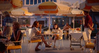 Movie still from “Beau Is Afraid” (2023), directed by Ari Aster – A woman and a man sitting at an outdoor table; Wide shot, High angle