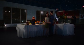 Movie still from “Beau Is Afraid” (2023), directed by Ari Aster – Two people standing in front of a table of food; Wide shot, High angle