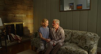 Movie still from “Beau Is Afraid” (2023), directed by Ari Aster – An older man and a younger woman sitting on a couch; Medium shot, Low angle