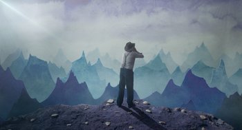 Movie still from “Beau Is Afraid” (2023), directed by Ari Aster – A man standing on top of a hill looking at a painting of mountains; Wide shot, Overhead angle