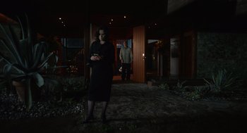 Movie still from “Beau Is Afraid” (2023), directed by Ari Aster – A woman standing in front of a man in front of a house; Wide shot, Low angle