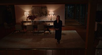 Movie still from “Beau Is Afraid” (2023), directed by Ari Aster – A woman standing in a living room on a rug; Extreme Wide shot, High angle