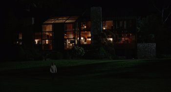 Movie still from “Beau Is Afraid” (2023), directed by Ari Aster – A man standing in the grass in front of a building at night; Extreme Wide shot, Low angle