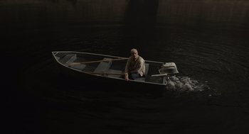 Movie still from “Beau Is Afraid” (2023), directed by Ari Aster – A man is sitting in a boat in the middle of the water; Wide shot, High angle