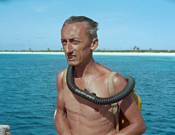 Movie still from “Becoming Cousteau” (2021), directed by Liz Garbus – An older man wearing a diving mask and a life buoy; Medium shot, High angle