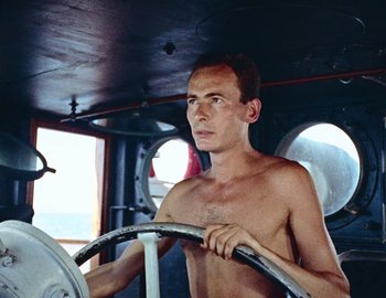 Movie still from “Becoming Cousteau” (2021), directed by Liz Garbus – A shirtless man driving a boat on the water; Close Up shot, Low angle