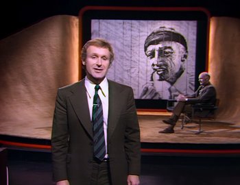 Movie still from “Becoming Cousteau” (2021), directed by Liz Garbus – A man standing in front of a painting of a man smoking a cigarette; Medium shot, Over the shoulder angle