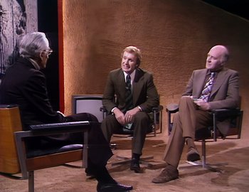 Movie still from “Becoming Cousteau” (2021), directed by Liz Garbus – Three men in suits are sitting in chairs and talking; Wide shot, High angle
