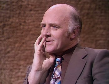 Movie still from “Becoming Cousteau” (2021), directed by Liz Garbus – An older man wearing a suit and tie with his hand to his face; Close Up shot, Low angle