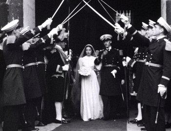 Movie still from “Becoming Cousteau” (2021), directed by Liz Garbus – An old photo of a bride and groom being guarded by a group of men; Wide shot, High angle