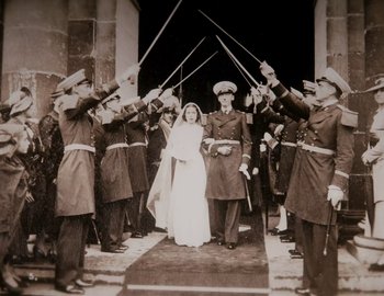 Movie still from “Becoming Cousteau” (2021), directed by Liz Garbus – An old photo of a woman in a wedding dress surrounded by men in uniform holding swords; Wide shot, High angle