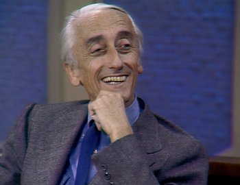 Movie still from “Becoming Cousteau” (2021), directed by Liz Garbus – An older man in a suit and tie smiling; Close Up shot, High angle