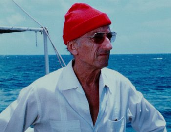 Movie still from “Becoming Cousteau” (2021), directed by Liz Garbus – An older man wearing a red hat on a boat in the ocean; Close Up shot, Low angle