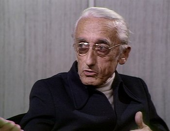 Movie still from “Becoming Cousteau” (2021), directed by Liz Garbus – An older man wearing glasses and a black jacket; Close Up shot, Over the shoulder angle