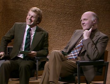 Movie still from “Becoming Cousteau” (2021), directed by Liz Garbus – Two men in suits and ties sitting in chairs; Medium shot, Over the shoulder angle
