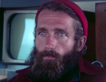 Movie still from “Becoming Cousteau” (2021), directed by Liz Garbus – A man with long hair and a beard wearing a red hat; Close Up shot, Low angle