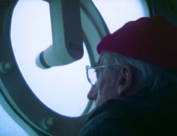 Movie still from “Becoming Cousteau” (2021), directed by Liz Garbus – An older man wearing glasses and a red hat; Close Up shot, Low angle