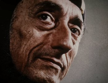 Movie still from “Becoming Cousteau” (2021), directed by Liz Garbus – An older man with a hat on his head looking up; Extreme Close Up shot, Low angle