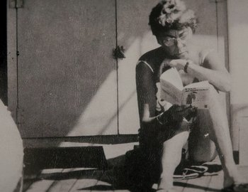 Movie still from “Becoming Cousteau” (2021), directed by Liz Garbus – A man sitting on the ground reading a book; Close Up shot, Overhead angle