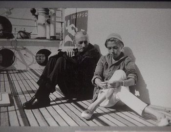 Movie still from “Becoming Cousteau” (2021), directed by Liz Garbus – A man and a woman sitting on a dock; Medium shot, High angle