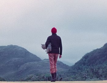 Movie still from “Becoming Cousteau” (2021), directed by Liz Garbus – A person with a red hat is holding a cat; Wide shot, Low angle