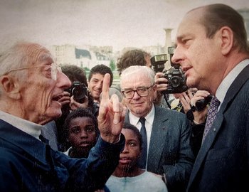 Movie still from “Becoming Cousteau” (2021), directed by Liz Garbus – A man giving a high five to another man in front of a group of people; Medium shot, Over the shoulder angle