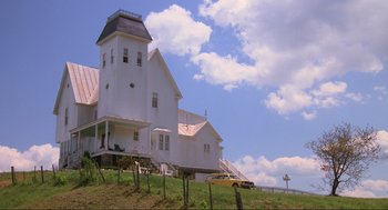 Movie still from “Beetlejuice” (1988), directed by Tim Burton – A white house sitting on top of a green hill; Extreme Wide shot, Low angle