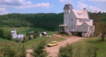 Movie still from “Beetlejuice” (1988), directed by Tim Burton – A yellow car parked in front of a white house; Extreme Wide shot, High angle