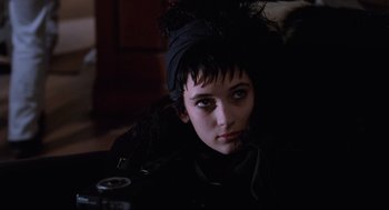 Movie still from “Beetlejuice” (1988), directed by Tim Burton – A woman with a black headscarf is sitting in a dark room; Close Up shot, Over the shoulder angle