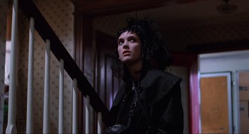 Movie still from “Beetlejuice” (1988), directed by Tim Burton – A woman in a black outfit standing next to a staircase; Medium shot, Low angle
